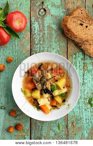Homemade chorba soup with lamb meat on bone potato carrots bay leaf and dried apricots served with basil and tomatoes overhead view