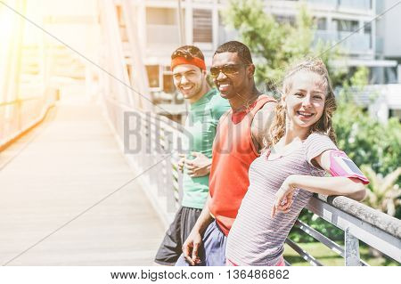 Young people runners resting after workout session on sunny day - Multi ethnic fitness friends taking break from running workout - Jogging and healthy lifestyle concept - Soft focus on girl