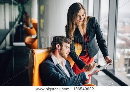 Group of business people, a man in a suit and a woman in a red dress and jacket, holding a tablet, winter city landscape outside the window on the background