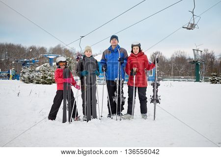 Family portrait of four skiers standing with skis at ski resort.