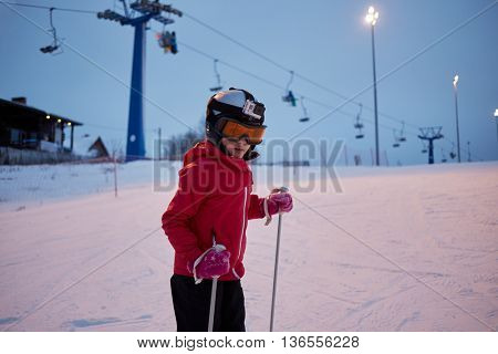 Girl in helmet with camera skiing on snowy slope at ski resort in evening. 