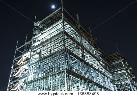 night view of metal framework of tall building under construction with lights illuminating detail