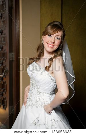 A three quarter pose of a beautiful bride. She is slightly turned ot the side holding her dress in one hand with her hip pushed out.