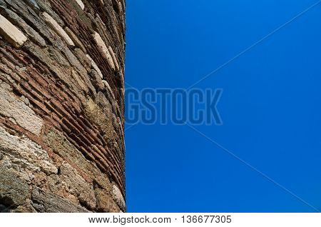 Ancient rough stone tower texture against clear blue sky. Abstract background with copy space