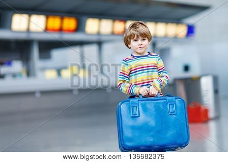 Cute little kid boy with blue suitcase on international airport. Happy child wating for flight and going on vacations.