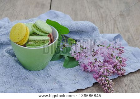 Sweet macaroons in porcelain teacups on a white crocheted napkin and lilac flowers