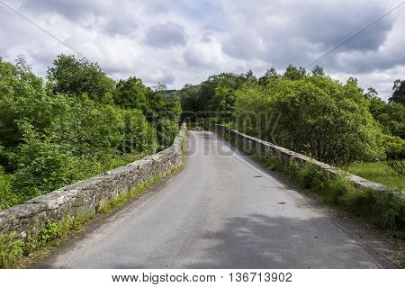 Ancient single track stone hump back bridge over the River Balvag at Balquhidder Scotland.