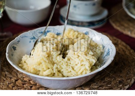 Traditional German Spaetzle, egg noodles made by pouring batter through a colander into boiling water, served in a rustic frying pan with blue and white checked cloth on a dark background