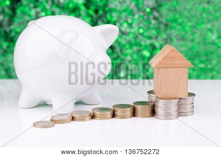 Wooden block houses and coin stacks in a row with a green background and a piggy bank