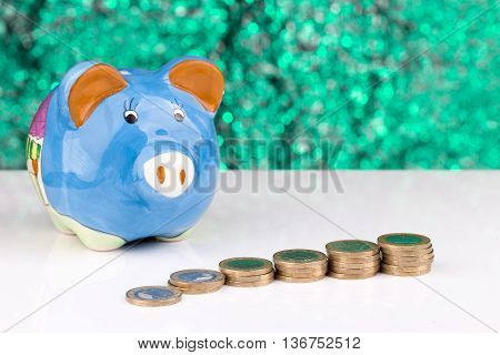 Blue piggy bank with a stack of coins and a green background