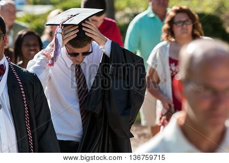 ATHENS, GA - MAY 2016:  A male graduate adjusts his mortarboard and tassle as he walks toward the graduation ceremony at the University of Georgia in Athens GA on May 13 2016.