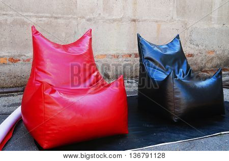 Beanbag of red and black color made ​​of shiny material on the background of gray wall