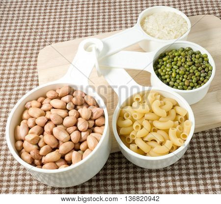 Foods High in Carbohydrate Raw Pasta Rice Peanuts and Mung Beans in Plastic Measuring Spoons.