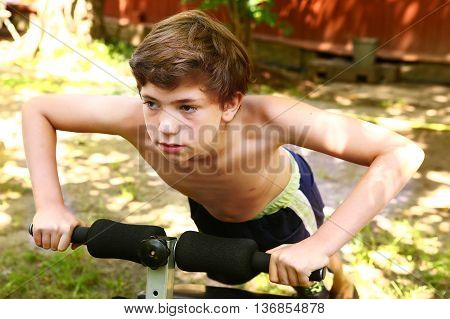 preteen handsome boy make push up on portable trainer in the open air garden yard close up photo