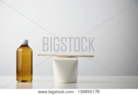 Retail takeaway presentation business set: plastic brown bottle with water on left side of closed blank noodles box with wok noodles inside and chopsticks on top isolated on white