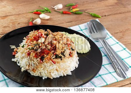 Rice topped with stir fried crab meat and basil in black dish on white wood