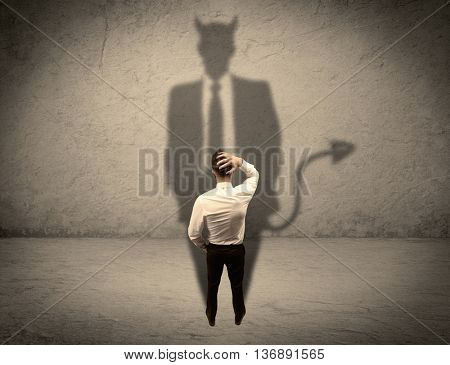 An experienced tricky businessman in suit looking at his devil desguise shadow reflected on the wall concept