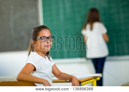 Two girls in the classroom one writes on the blackboard and the other sitting at the table