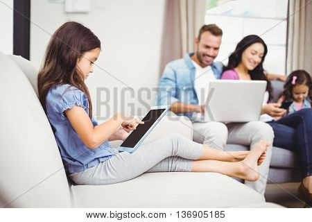 Close-up of girl using digital tablet on sofa while family in background at home