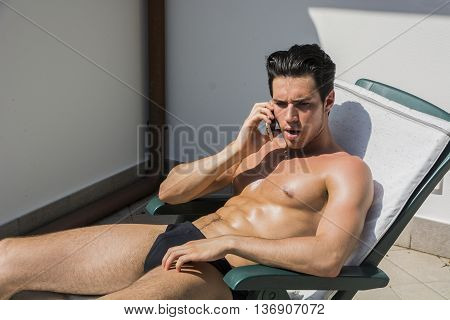 Shirtless Young Man Drying Off in Hot Sun Talking on Cell Phone, Muscular Man Wearing Bathing Suit Sunbathing on Beach Lounge Chair, Eyes Closed