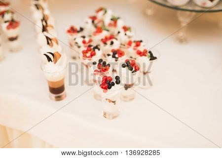 Delicious and tasty dessert table with cupcakes and shots at reception closeup.