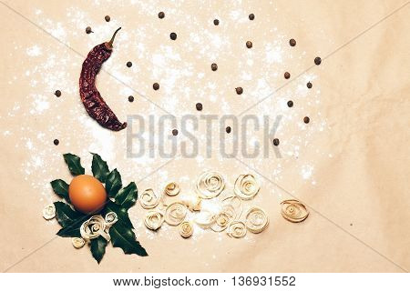 Natural background with egg on laurel leaves red chili pepper allspice excelsior on pack paper decorated with white flour copyspace