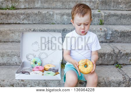 child sitting on the steps with a box of donuts. little boy playing with a donut. concept of junk food for kids. take out food
