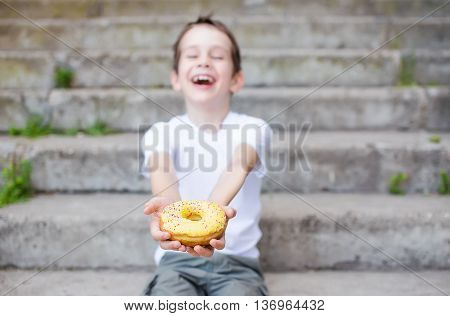 laughing boy holding a donut. boy sitting on the steps with a donut in his hand and he having fun. selective focus