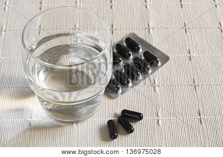 Medical capsules with activated charcoal and glass of water on tablecloth