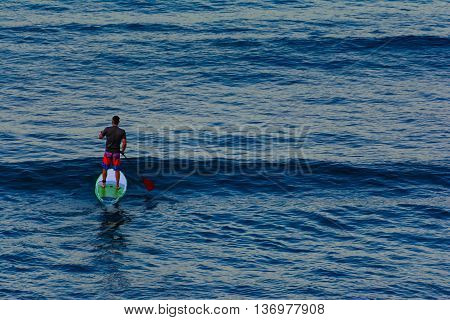 Lone Paddleboarder on the water at dawn. Calm blue water with rolliing waves