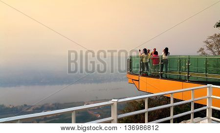 Nong Khai province Thailand- April 28 2016: Tourists walking and taking photograph on transparent sky walk to see view of Mekong River during sunset at Wat Pha Tak Suea Sangkhom district Nong Khai province Thailand.