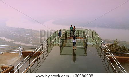 Nong Khai province Thailand- April 28 2016: Tourists walking and taking photograph on transparent sky walk to see view of Mekong River during sunset at Wat Pha Tak Suea Sangkhom district Nong Khai province Thailand.