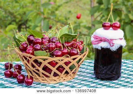 Basket of cherries and cherry jam jar on background of cherry tree