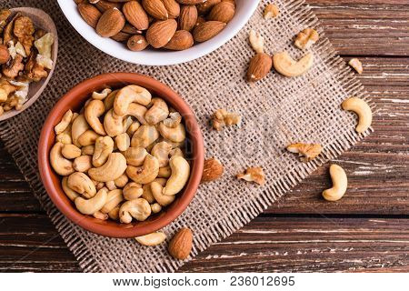 Differrent Variety Of Nuts - Walnuts, Cashew, Almond In Bowls. Rustic Scratched Wooden Table Backgro