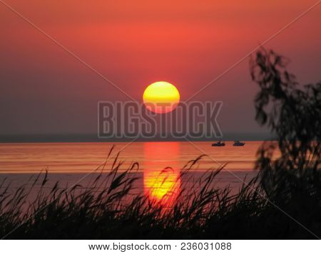 Sea Bay At Sunset With A Bright Sky, Great Sun And Its Reflection In The Water, Dark Silhouettes Of 