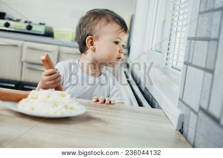 Handsome Boy Shaggy And Shkod Eats Sausage In The Kitchen In A White T-shirt In The Afternoon And Lo