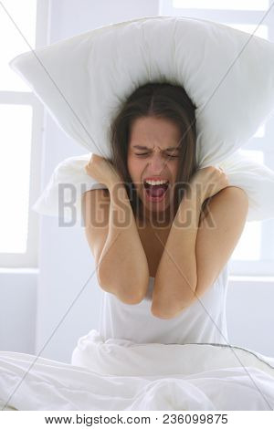 Young caucasian woman covering her head and ears with pillows