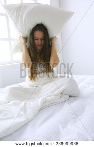 Young caucasian woman covering her head and ears with pillows