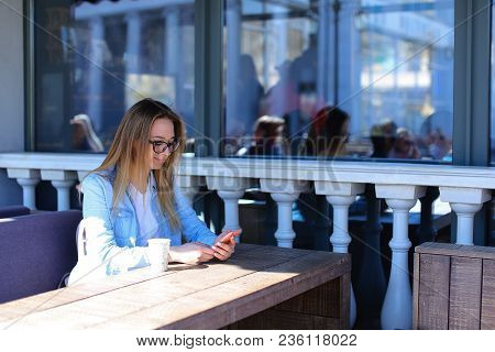 Young Female Peson Resting At Street Cafe With Smartpnone In Pink Case. Concept Of Using Hortspot An