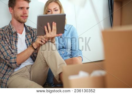Young couple moving in new home.Sitting and relaxing after unpacking.Looking something on laptop. Young couple