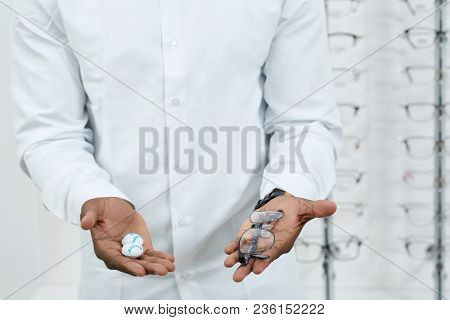 Man In White Shirt Is Keeping Optical Eyeglasses Standing In Front Of Transparent Stand With Differe