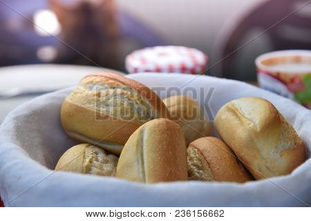 Basket Of Freshly Baked Dinner Rolls With Tableware In Background. Close Up