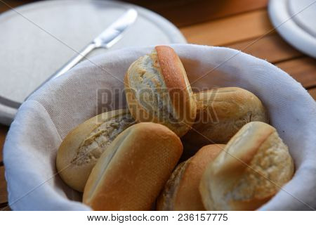 Basket Of Freshly Baked Dinner Rolls With Tableware In Background. Close Up
