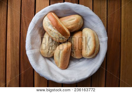 Basket Of Freshly Baked Dinner Rolls With Tableware In Background. Close Up