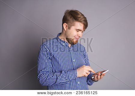 Young Man Texting Message On Smart Phone Isolated On Grey Background. Smiling Guy Holding Smartphone