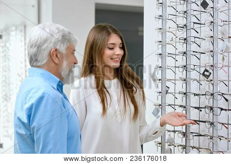 Sideview Of Smiling Assistant Showing Eyeglasses To Old Patient. Advising Which Optical Glasses Are 