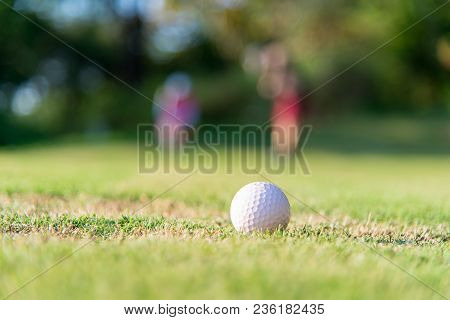 Golf Ball Approach To The Hold On The Green. Couple Golf Player Ptiching Golf Ball In The Background