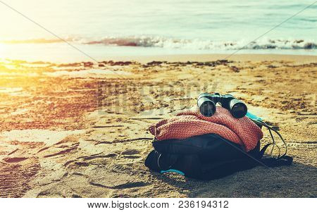 Travel Aventure Concept. Binoculars And Hiking Backpack Lie On The Sunshine Seashore