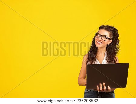 Young Positive Cool Lady With Curly Hair Holding Laptop Looding Away Daydreaming And Smiling Isolate