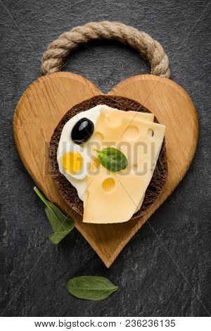 Open  faced cheese sandwich canape or crostini on a wooden serving board  on dark stone background closeup. Top view.